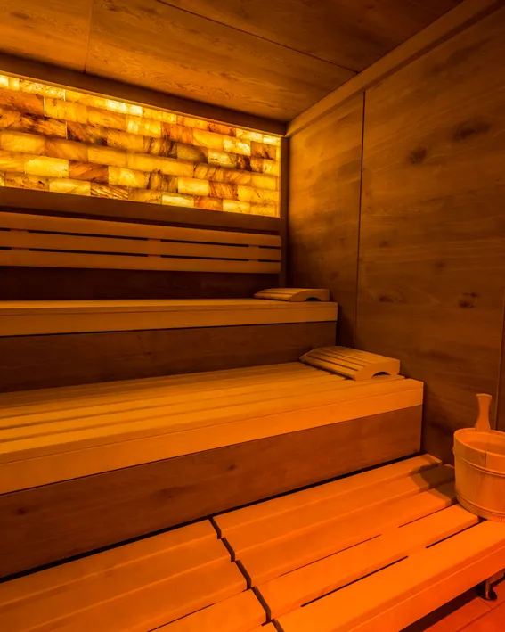 Moderne Holzsauna mit warmer Beleuchtung und einem Eimer auf der Bank